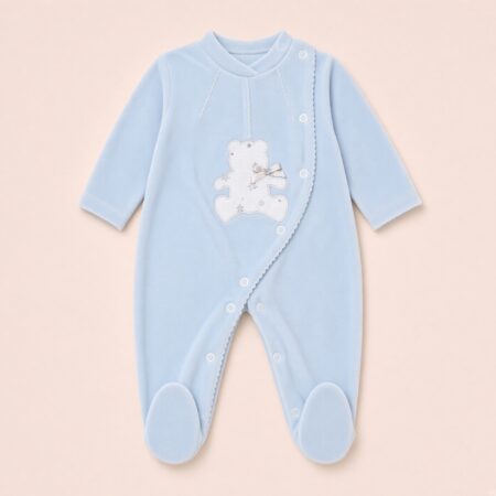 Babygrow de bebé em veludo azul claro com aplique de urso branco e laço, abertura lateral com botões, mangas compridas e pés fechados